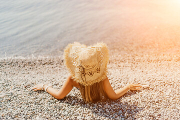 Beach Relaxation woman in hat sits on a pebble beach enjoying the sunshine. The concept of travel,...