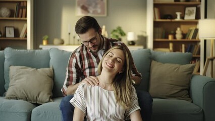 Caring young man massaging his girlfriend's neck in her menstrual period while sitting at home. Shot in slow-motion