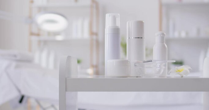 White bottles, cream jars and cosmetic skin care products for female skin and body care in empty beauty spa salon room. Spa treatment, wellness and cosmetology concept. 4k video. Slow motion video.