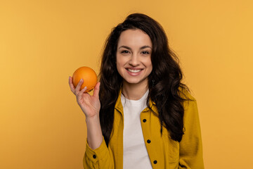 Cheerful beautiful dark-haired young female smiling at the camera with citrus fruit in her hand....