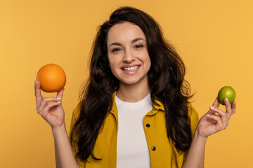 Joyous young woman posing for the camera with a couple of citrus fruits on the yellow background....
