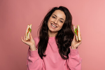 Cheerful young pretty woman showing her favorite appetizing nourishing sandwiches during the studio...