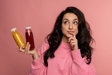 Pensive young brunette with a pair of bottled soft beverages posing for the camera on the pink background. Healthy drink concept