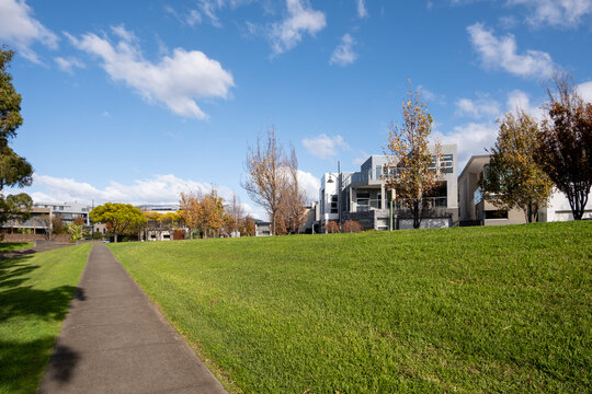 A pedestrian footpath leads to a clean neighbourhood in Melbourne, Australia. A beautiful natural environment in the suburb, with houses lined the street and a well-maintained grass lawn in park. 