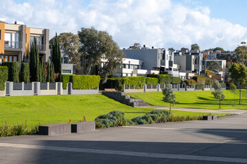 A row of modern and contemporary-style houses facing a large urban park with a concrete walkway and...