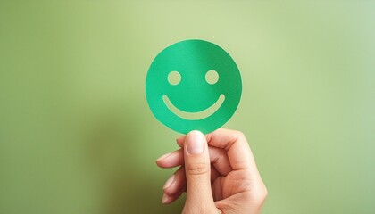 Hand holding green paper cut happy smile face on green background , positive thinking