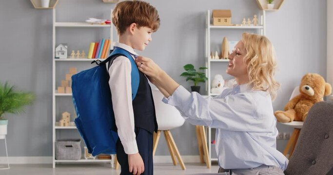 Caring Parent, Loving Mother Helping Happy Pupil Kid In Uniform, Put Backpack, Preparing Go To School Standing Home Room, Dressing, Getting Child Son Ready In Morning At Home Before Happy School Day 