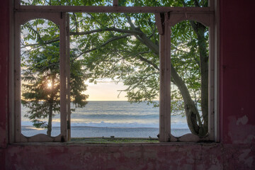 View of a sunset seascape from broken window in an abandoned house with pink walls