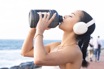 Girl with white headphones playing sports, hydrating, drinking water