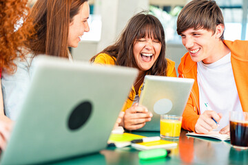 University students sitting together at table with books and laptop - Happy young people doing group study in high school library - Life style concept with guys and girls in college campus