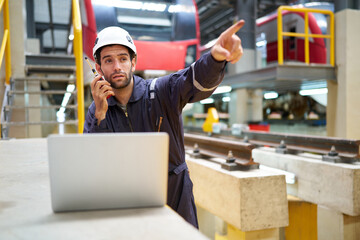 Engineer or worker working on laptop computer and talking on walkie talkie at construction train station