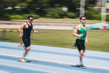 Two men are running on a track. They are on the finishing straight of a race