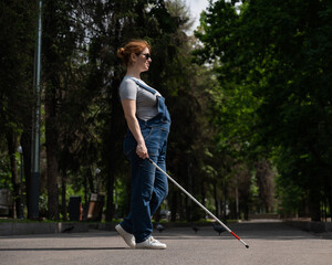 Blind pregnant woman crosses the street with the help of a tactile cane.