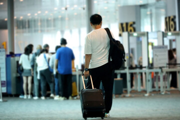 Asian man carrying suitcase on trolley in airport hallway rushing towards departure gate. concept...