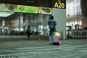 Rear view of a male traveler carrying a suitcase walking in the airport corridor towards the plane departure gate. concept of traveling by air transport.