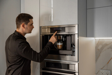 Young man using modern built-in coffee machine in kitchen