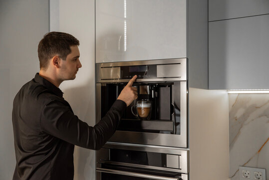 Young man using modern built-in coffee machine in kitchen