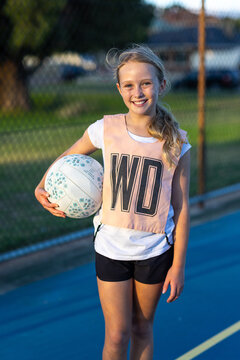 smiling young girl holding netball and wearing WD wing defence bib on netball court