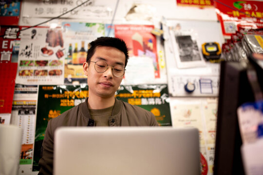 Happy Asian grocery store manager working at laptop at the counter