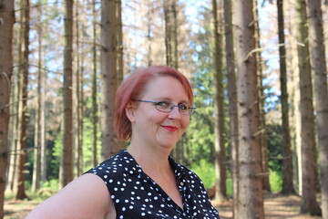 Portrait of a red-haired cheerful woman in the forest on a beautiful sunny summer day