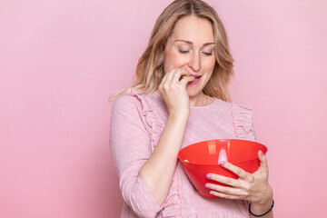 Woman Eating Snacks from Red Bowl on Pink Background
