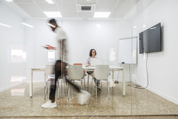 Blurred Man Walking Past Conference Room With Woman Working at Table