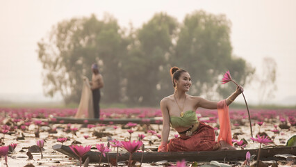 Young Asian women in Traditional dress in the boat and pink lotus flowers in the pond. Beautiful...
