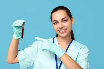 Portrait of female doctor pointing at test tube with blood sample on blue background