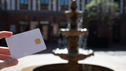 A person holding a white credit card in front of a fountain