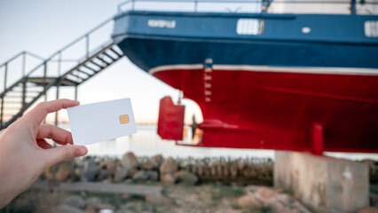 A person holding a credit card next to a boat
