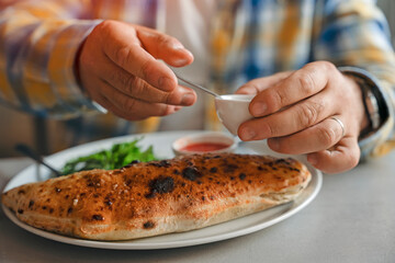 hands of man eating pizza calzone in cafe