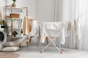 Interior of light laundry room with clean clothes hanging on dryer