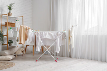 Interior of light laundry room with clean clothes hanging on dryer