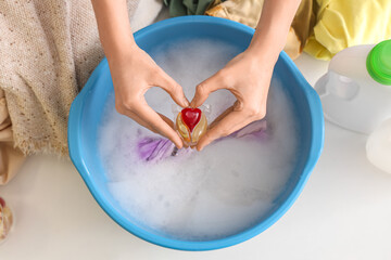 Woman putting capsule of laundry detergent in plastic basin