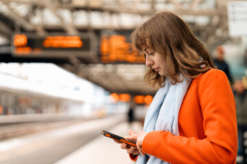 young woman traveler using phone  waiting fortrain at railway station on platform	