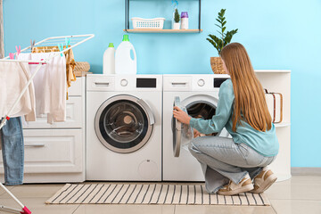 Woman putting clothes into washing machine in laundry room, back view