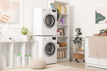 Interior of light laundry room with washing machines, cleaning supplies and houseplants