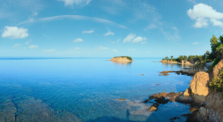 Morning Aegean Sea rocky coast view with shadow of photographer on clear water surface (Nikiti, Sithonia, Halkidiki, Greece). Two shots stitch panorama.