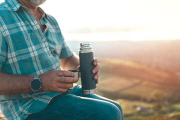 Man relaxing alone on top of mountain and drinking hot coffee at sunrise. Travel Lifestyle  