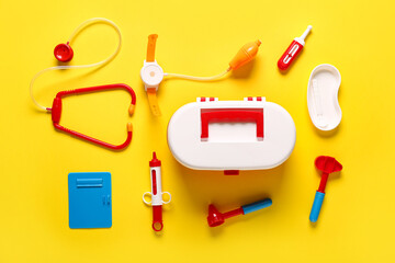 Toy first aid kit with stethoscope, thermometer and reflex hammer on yellow background. Top view