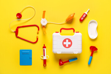Toy first aid kit with stethoscope, thermometer and reflex hammer on yellow background. Top view