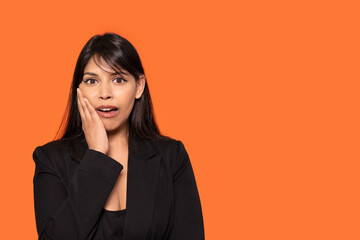 Woman with hand on cheek hearing unbelievable news on orange background