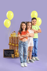 Cute little children near lemonade stand on lilac background