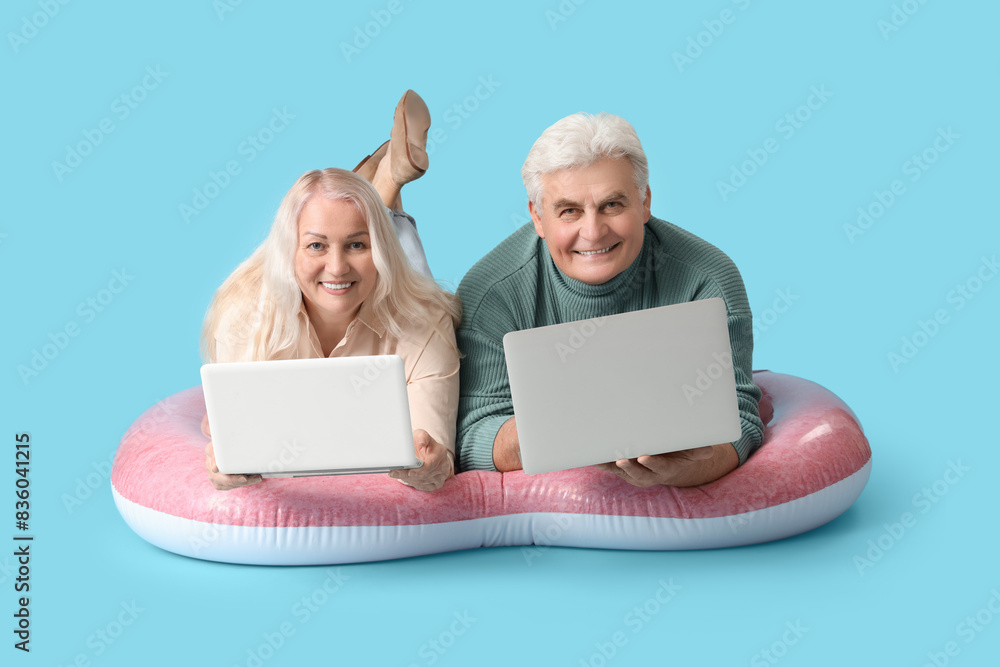 Wall mural Mature couple with laptops on swim mattress ready for summer vacation against blue background