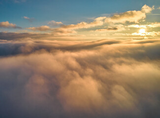 Fog spreads over the mountains at dawn. The sun rises on the horizon. Carpathians in the morning. Aerial drone view.
