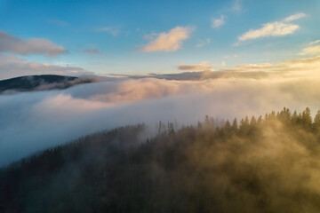 Fog spreads over the mountains at dawn. The sun rises on the horizon. Carpathians in the morning. Aerial drone view.