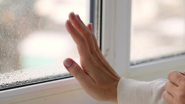 Woman checking with her hand cold draft from the glasses of window. Condensation on the windows glass. 4K