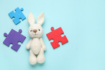 Colorful puzzle pieces and toy bunny on blue background. Concept of autistic disorder. Top view
