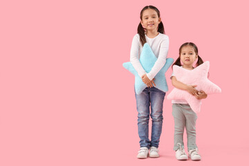 Cute little Asian happy sisters with pillows in shape of stars on pink background