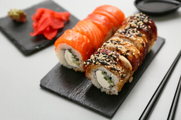 Board with tasty sushi rolls and chopsticks on grey background, closeup